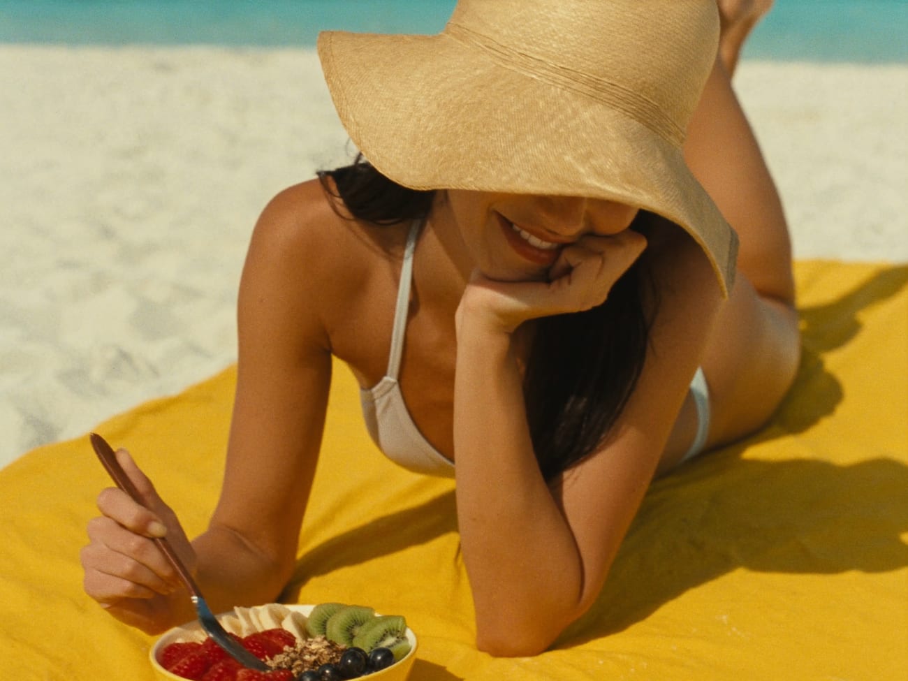 Frau am Strand auf einem gelben Handtuch mit einer Bowl